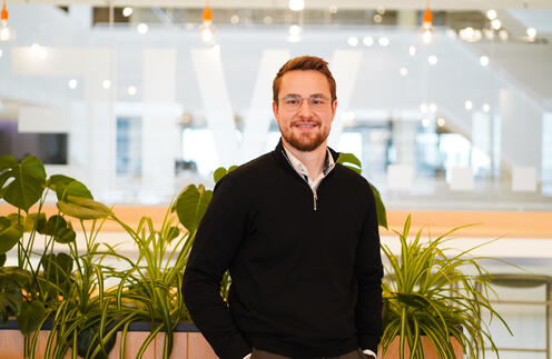 Unser Kollege steht vor mehreren Pflanzen und lächelt in die Kamera